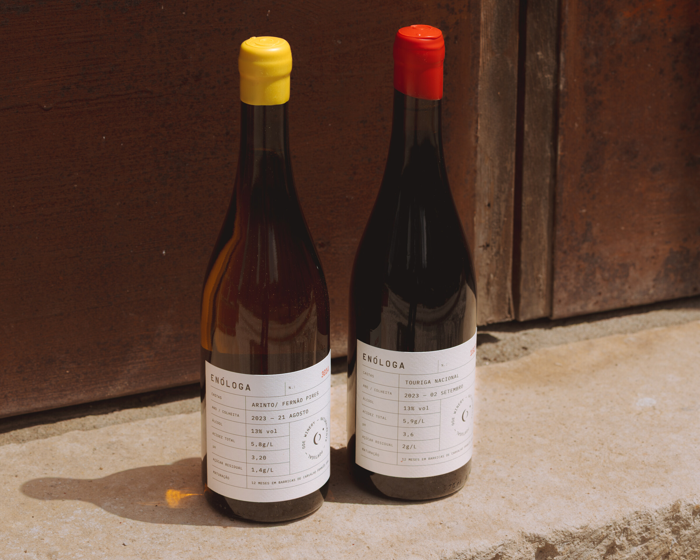Two ODE Enóloga bottles against a rustic wooden door.